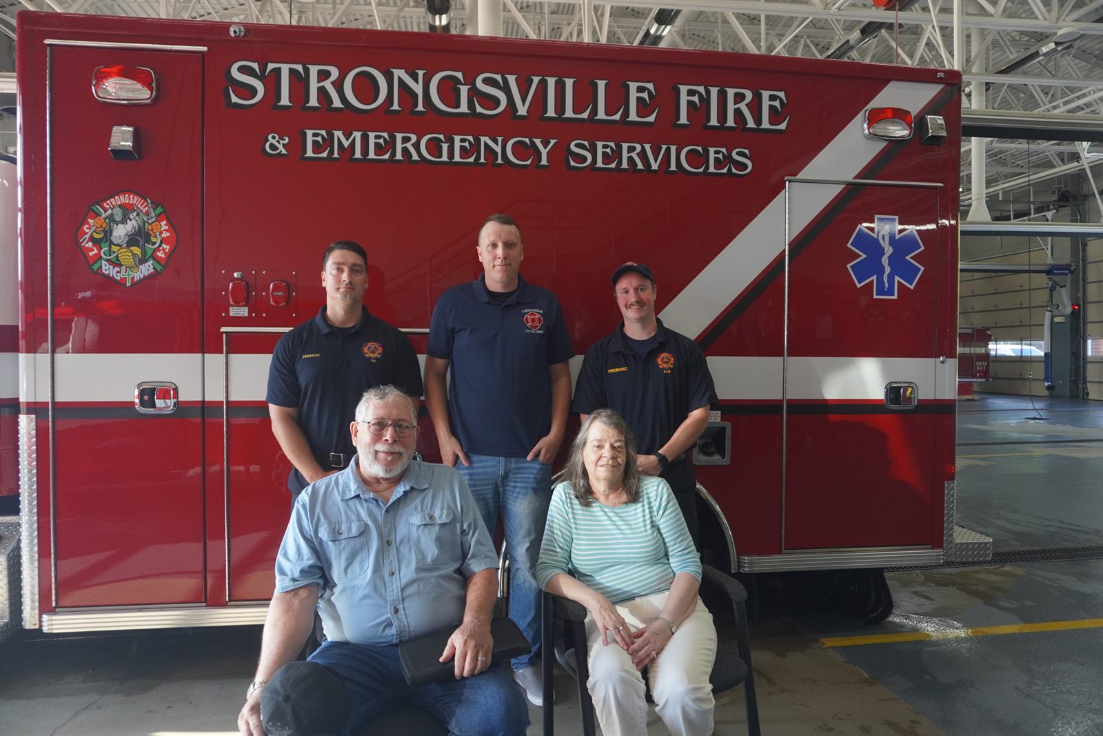 Angela and Marc Wintermute seated in front of a Strongsville Fire ambulance with firefighter/paramedics Jason March, Lee Brass and Matt Janosek